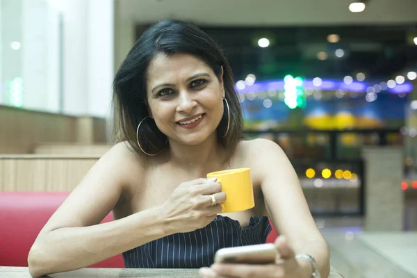 Mujer bebiendo café y usando el teléfono móvil en la cafetería — Foto de Stock