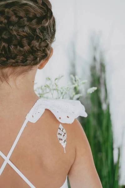 Başında Braid Crown saç stili var. Omzunda tercüme edilebilir bir dövme var. Tüy şeklinde bir dövme..