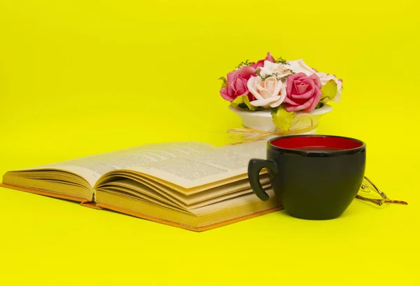 Black cup with hot tea and book on the yellow background