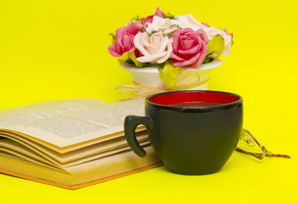 Black cup with hot tea and book on the yellow background