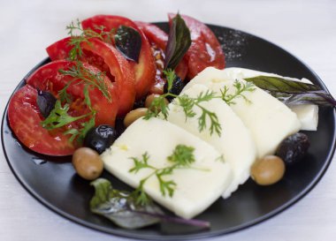 Beyaz peynir domates, yeşil ve siyah zeytin, fesleğen, kişniş ve zeytinyağı siyah plaka üzerinde