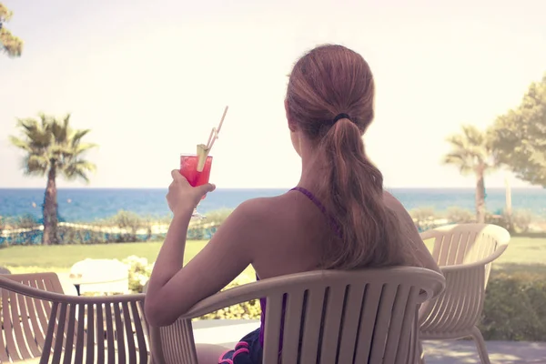 Young girl with red cocktail in her hand sits at a bar by the sea
