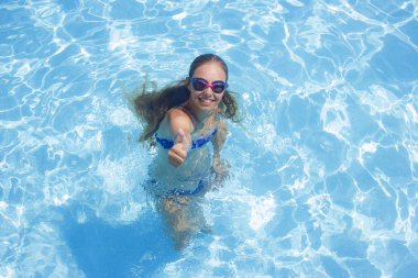 Neşeli kız gülümseyerek ve başparmak gösterilmesini havuzu