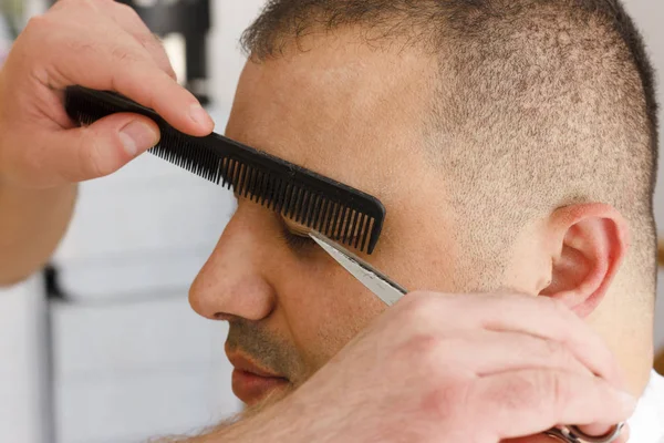 Scissors cutting eyebrow of man at the barbershop. Brow grooming close up.