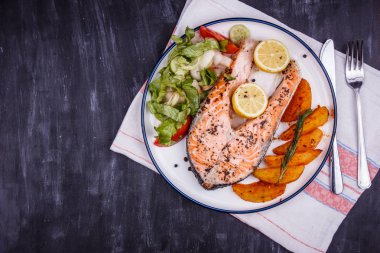 Siyah ahşap masada limon, patates, salata ve baharatlar ile kızarmış somon