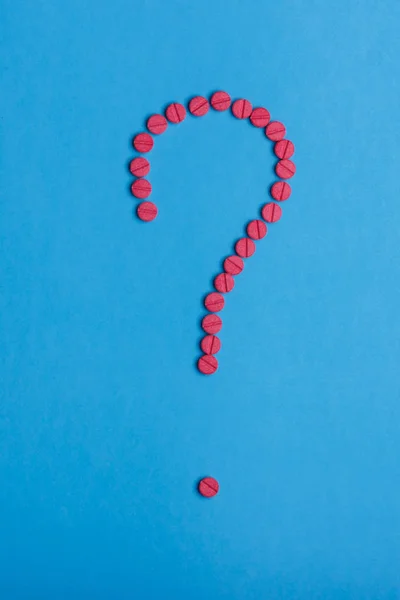 Знак вопроса, сделанный из красных таблеток на синем фоне — стоковое фото