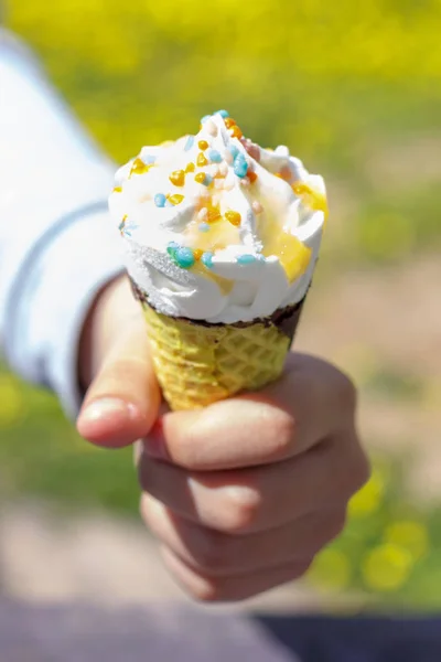 Hand holds ice cream in a waffle cone in summer under the sun. Selective focus