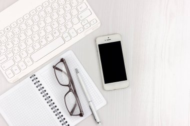 Dizüstü bilgisayar, akıllı telefon, gözlük, dizüstü bilgisayar ve kopya alanı arka plan ile kalem ile beyaz ofis masası düz yatıyordu. Mockup