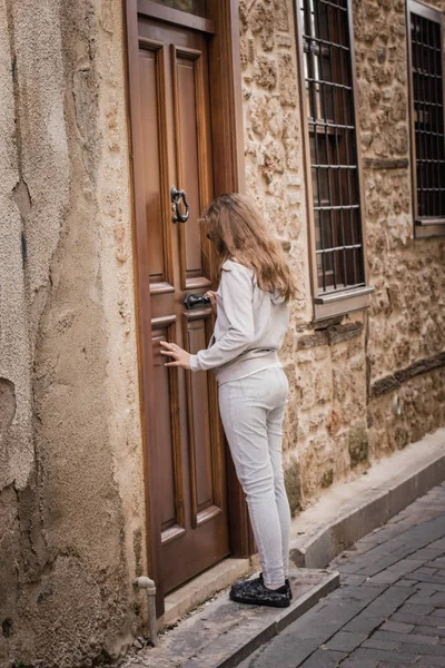 若い女の子はアンタルヤの旧市街の狭い通りに古い木製のドアをノックしています — ストック写真