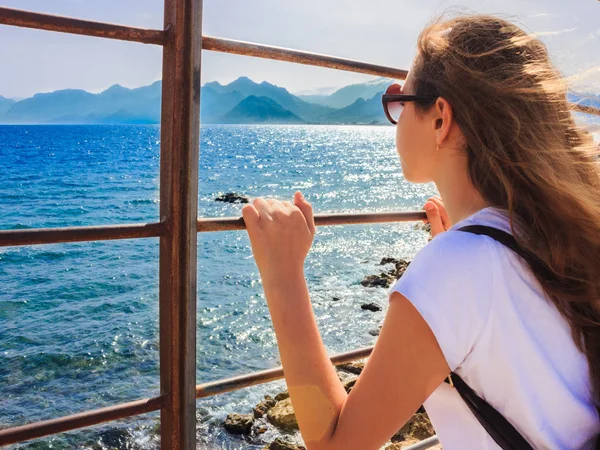 Young girl with long hair looks at the blue sea through the bars — Stockfoto