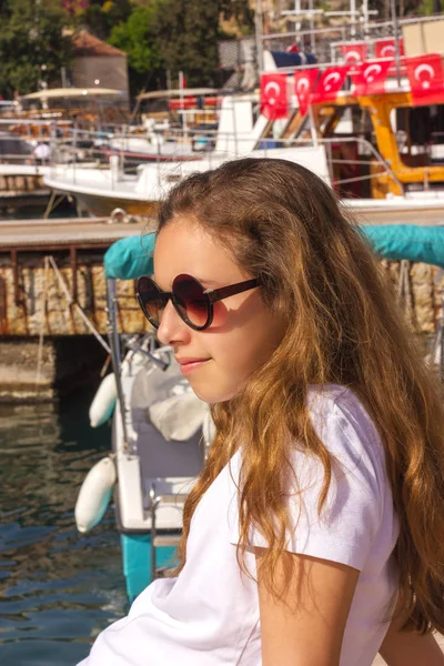 Mladá dívka s dlouhými vlasy sedí na molu v přístavu jachty a dívá se na modré moře — Stock fotografie