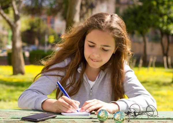 Schattig tiener meisje schrijft notities op een papieren pad door houten tafel op een — Stockfoto