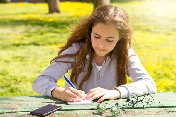 Cute teen girl writes notes on a paper pad by wooden table on a