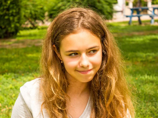 Yeşil çim parkta gülümseyen uzun saçlı güzel genç kız