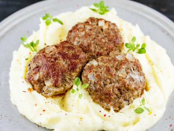 Mashed potatoes and meat balls on a gray plate, decorated with fresh basil
