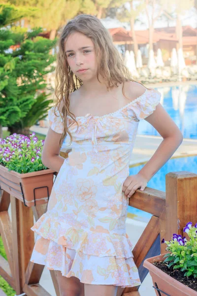 Nettes Teenie-Mädchen in einem romantischen Kleid und mit langen Haaren steht auf der Brücke am Pool — Stockfoto