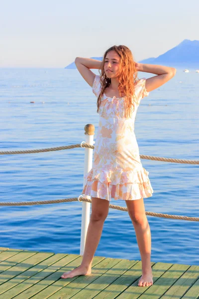 Linda chica adolescente en vestido y con el pelo largo en el muelle junto al mar —  Fotos de Stock