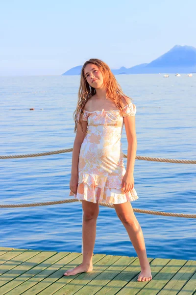 Linda chica adolescente en vestido y con el pelo largo en el muelle junto al mar —  Fotos de Stock