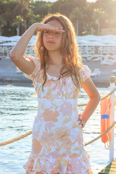 Hermosa adolescente en los rayos del sol poniente en un muelle junto al mar —  Fotos de Stock