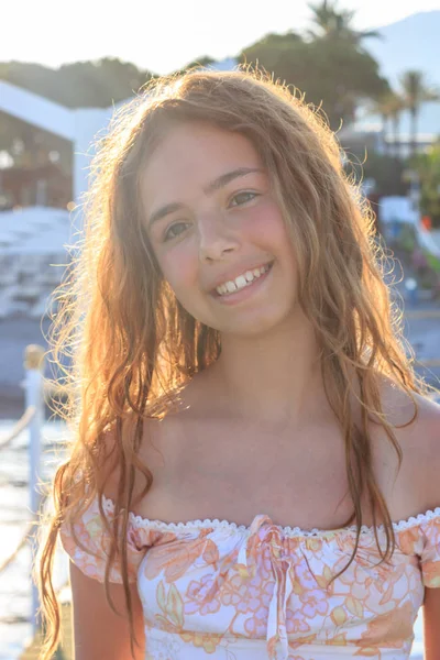 Schöne Teenager-Mädchen in den Strahlen der untergehenden Sonne auf einem Pier am Meer — Stockfoto