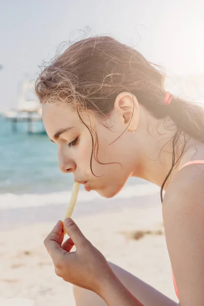 Νέος όμορφη έφηβος κορίτσι τρώει τηγανιτές πατάτες στην παραλία κοντά στη θάλασσα — Φωτογραφία Αρχείου