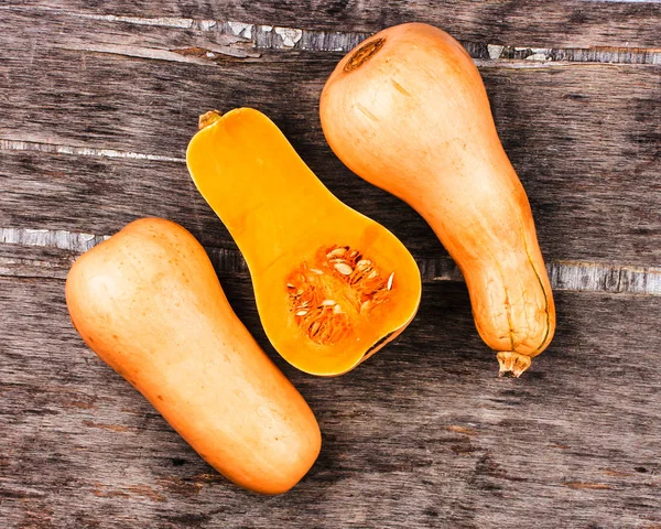 Kürbis auf schwarzem Holztisch. Drei orangefarbene Kürbisse in Birnenform. halber Kürbis in die Mitte geschnitten — Stockfoto