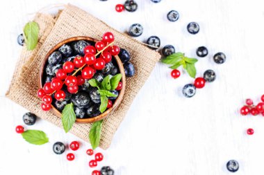 Taze yaban mersini ve nane yaprakları ile kırmızı kuş üzümü çuval üzerinde ahşap bir kase. Diyet gıda, vegan çilek