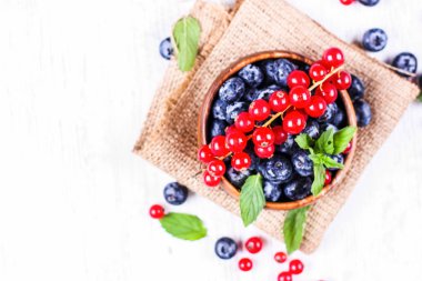 Taze yaban mersini ve nane yaprakları ile kırmızı kuş üzümü çuval üzerinde ahşap bir kase. Diyet gıda, vegan çilek