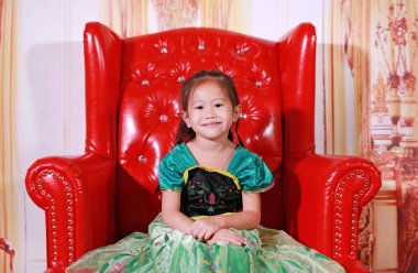 Sevimli küçük Asya kız ile antika arka plan üzerinde kırmızı kanepede oturan bir fantezi kıyafet giymiş.