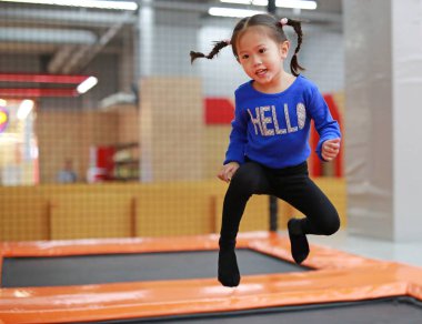 Küçük Asyalı çocuk kız, trambolin içinde kapalı Bahçesi atlama. Etkin kız eğlenmek spor merkezinde tatil.