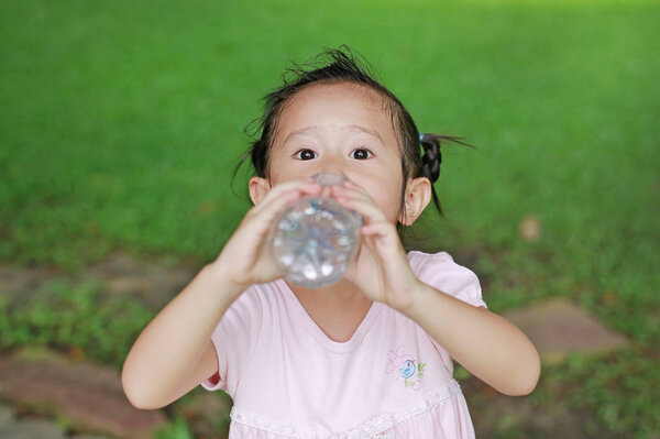 Закройте маленькую девочку, пьющую воду из бутылки в парке. Портрет открытый
.