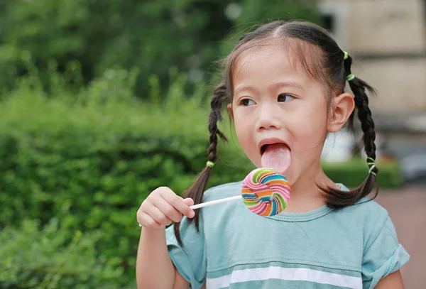 关闭小女孩舔棒糖糖果在花园里看出来 — 图库照片