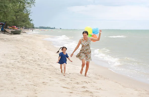 Portrait of Mother and daughter running on beach with colorful balloons in mother hand. Holiday concept.