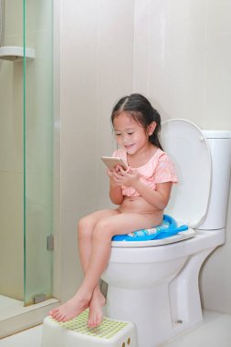 Tuvalette otururken ve smartphone birlikte arıyorsunuz küçük Asyalı çocuk kız.