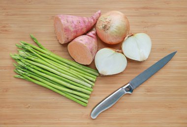 Taze yeşil kuşkonmaz, soğan ve tatlı patates ile ahşap tahta arka plan üzerinde keskin bıçak.