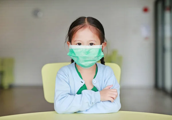 Sevimli küçük Asyalı çocuk kız çocuk odası çocuk sandalyede oturan bir koruyucu maske takarak.