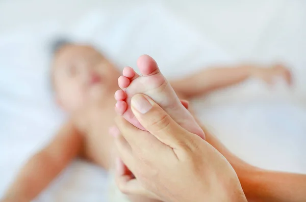 Mom making foot massage for her infant baby on the bed.