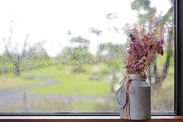 Boutique purple dried flower in the vase for home decoration against glass window with rain drop on rainy day.