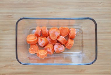 Ahşap tahta üzerinde kare cam kapta havuç küpleri turuncu kalp