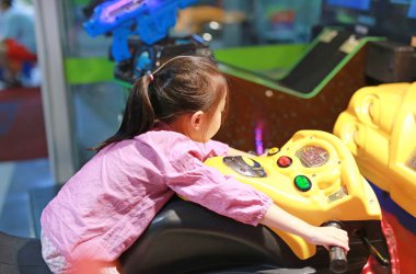 Arcade video oyunu oynarken küçük Asyalı çocuk kız yan görünüm. Motosiklet yarış.