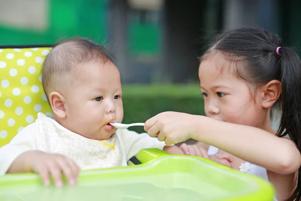 特写亚洲姐妹为她的小弟弟在花园的塑料椅上喂食物 — 图库照片