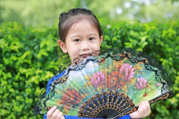 Portrait of little Asian child girl with holding Chinese style fan in the summer garden.