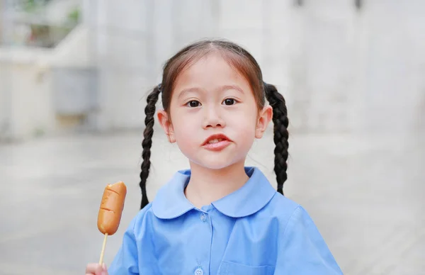 可爱的小亚洲儿童女孩在学校制服享受吃香肠 — 图库照片