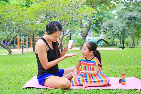 Mother appying body lotion for daughter\'s in the summer park.