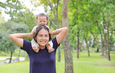 Güzel genç Asya anne doğa Park annemin omzuna at binme mutlu bebek çocuk ile.