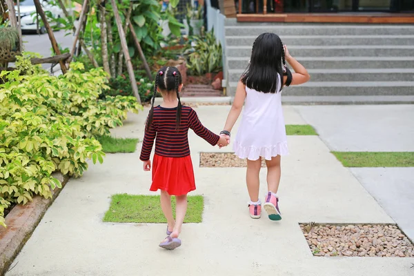 姐姐的后视图牵手与小孩子走在道路花园 — 图库照片