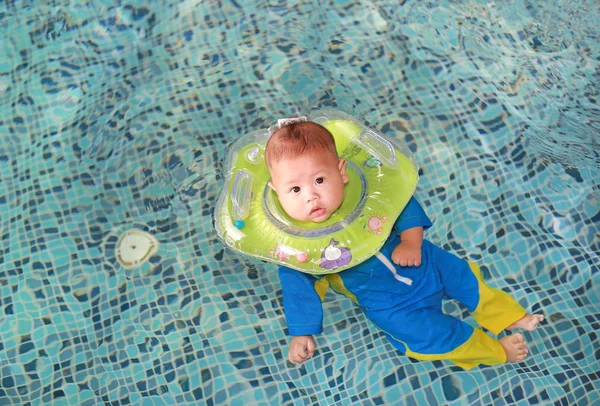 Infant baby boy training to swim in pool with safety by baby neck floats.