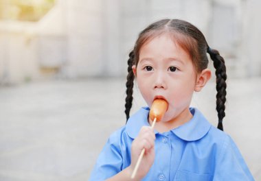 Okul tek tip, küçük Asyalı çocuk kız portresi zevk lezzetli sosis yeme.