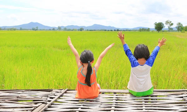 アジア子供の後姿の腕を伸ばすし 山と雲空と若い緑の田んぼに竹落葉の上に座ってリラックスして — ストック写真