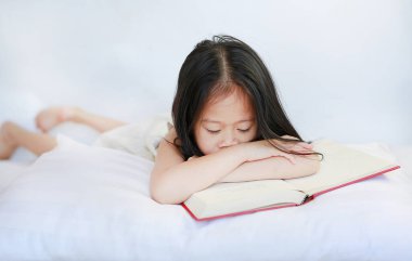 Küçük Asyalı çocuk kızla yastığın beyaz arka plan üzerinde yatan ciltli kitap okuma.
